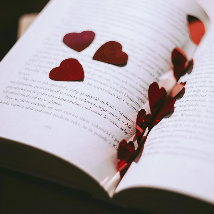 An open book adorned with red heart-shaped confetti, perfect for Valentine's or romantic themes.